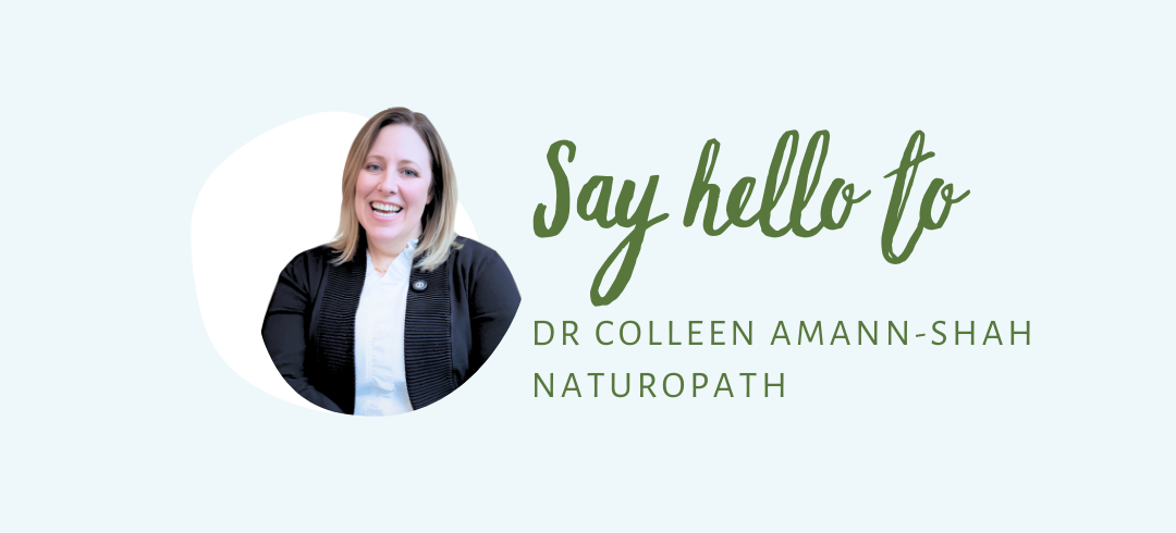 Smiling woman with shoulder-length blonde hair wearing a black blazer over a white shirt. She is framed in a soft white oval on a light green background. To her right, green cursive and uppercase text reads, 'Say hello to Dr. Colleen Amann-Shah, Naturopath.